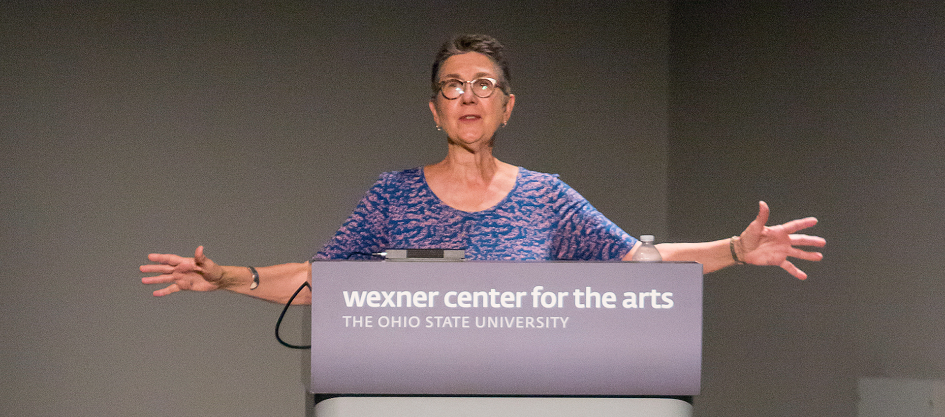 Julia Reichert stands at a podium with her arms outstretched