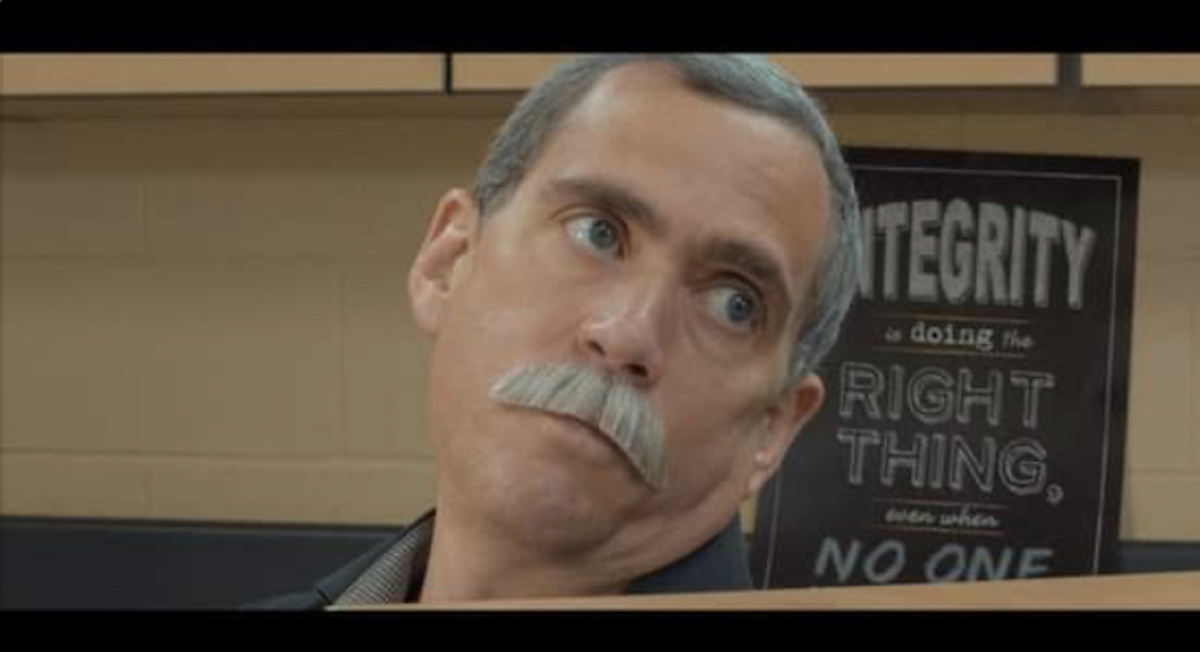 A man with short graying hair and a mustache sits in a courtroom. His eyes are turned to his left and slightly upward. He has a look of skepticism on his face.