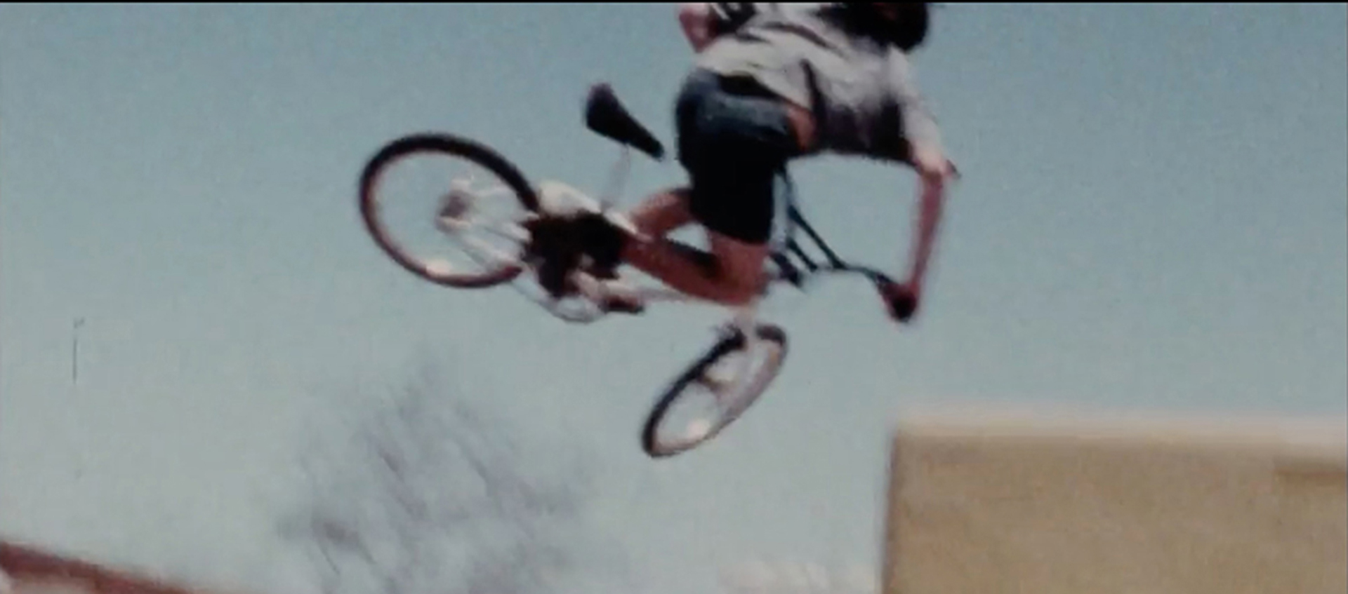 A blurry still featuring a person on a bike in the air over a skateboard ramp.