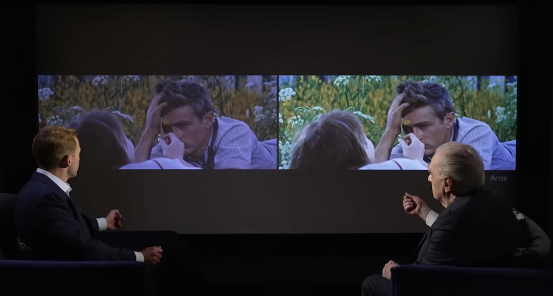 Two men sit in a darkened screening room. They’re looking away from the camera, at the screen between them that holds side-by-side images showing the differences between pre-restoration and post-restoration versions of the film Rebel Without a Cause.