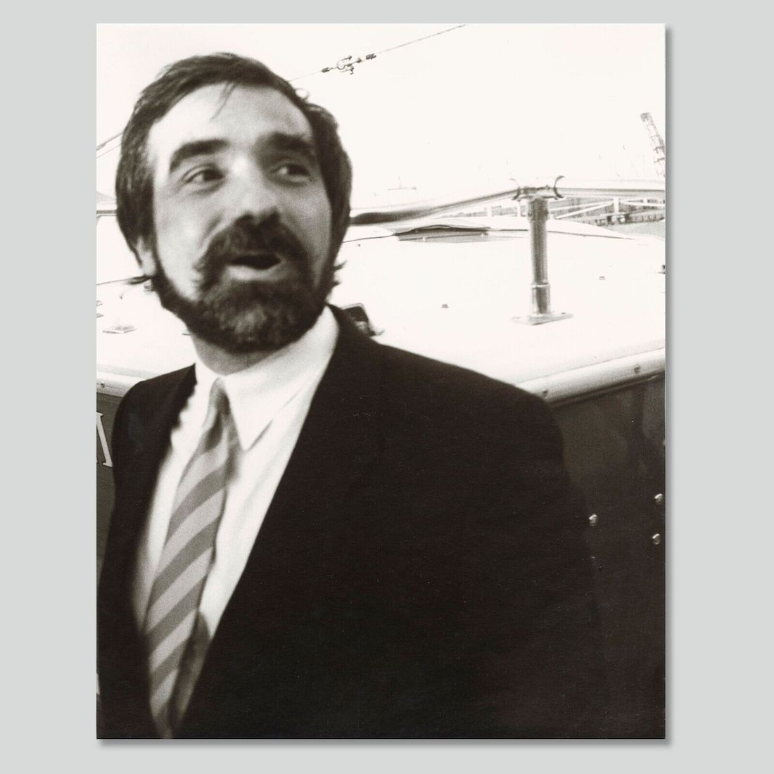 Black and white photograph of a man with short dark hair and a beard and mustache. He’s wearing a suit with a striped tie. He seems to be caught in the act of talking.