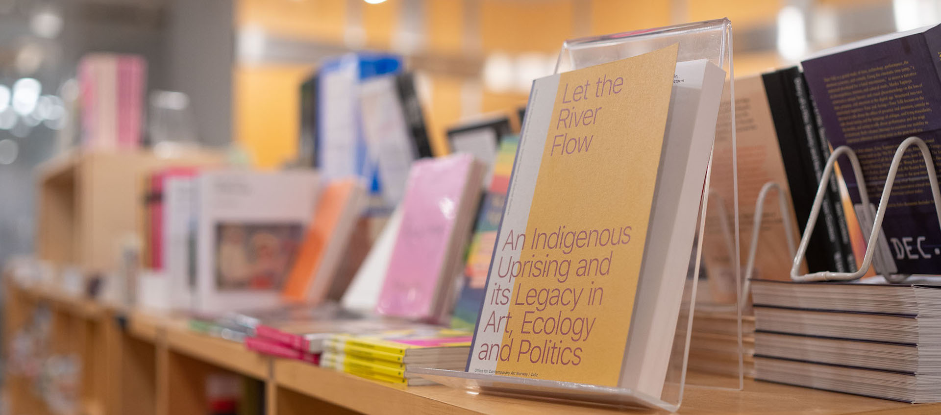 A row of books, some propped up and some resting flat, sit on top of light wood shelving in the Wexner Center Store. 