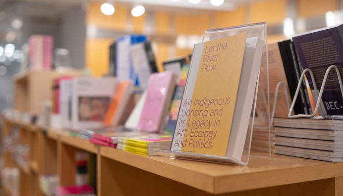 A row of books, some propped up and some resting flat, sit on top of light wood shelving in the Wexner Center Store. 