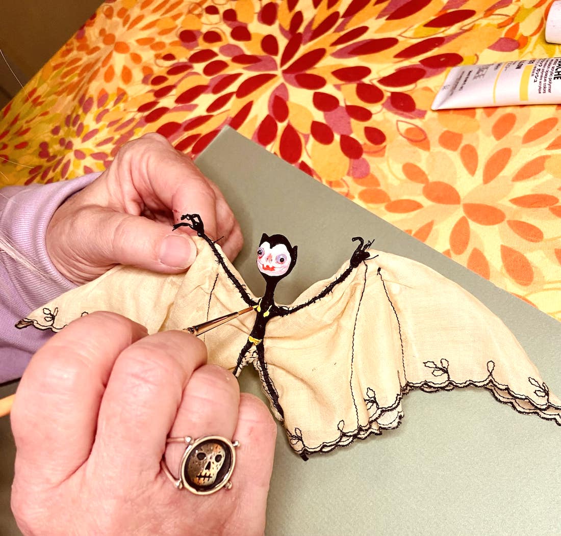 Close-up of two hands working on a small, painted and stitched fabric sculpture of a bat