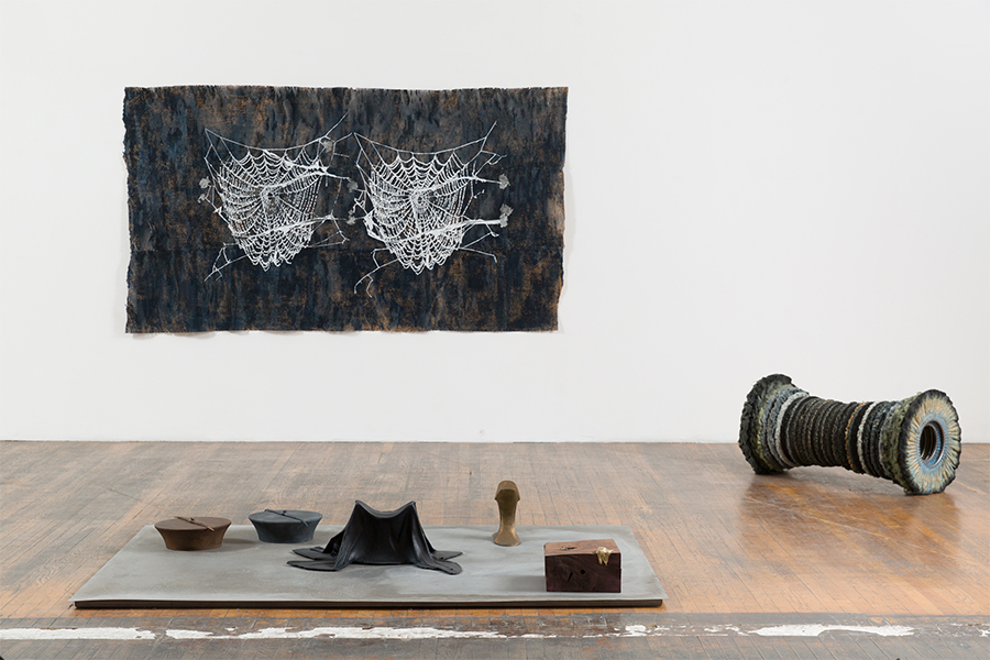 Two mixed-media sculptures on a wooden floor and a rectangular work with two hand-cut spiderweb silkscreens on a white wall.