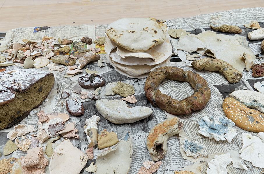 Overhead view of ceramic sculptures that look like different types of bread. The pieces are arranged on newspaper.