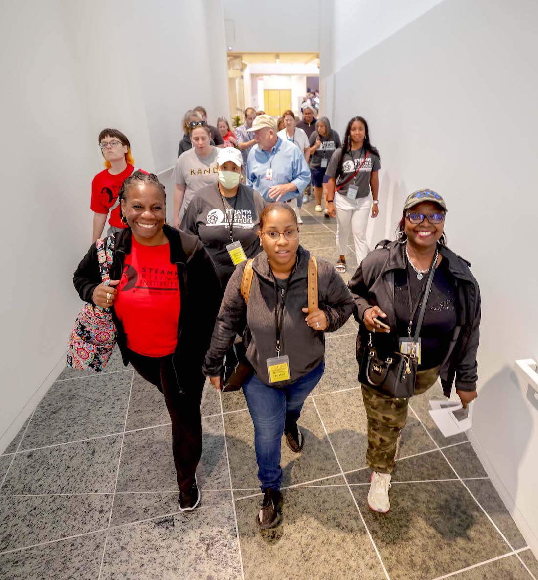 A group of over a dozen people walks up a narrow ramp.