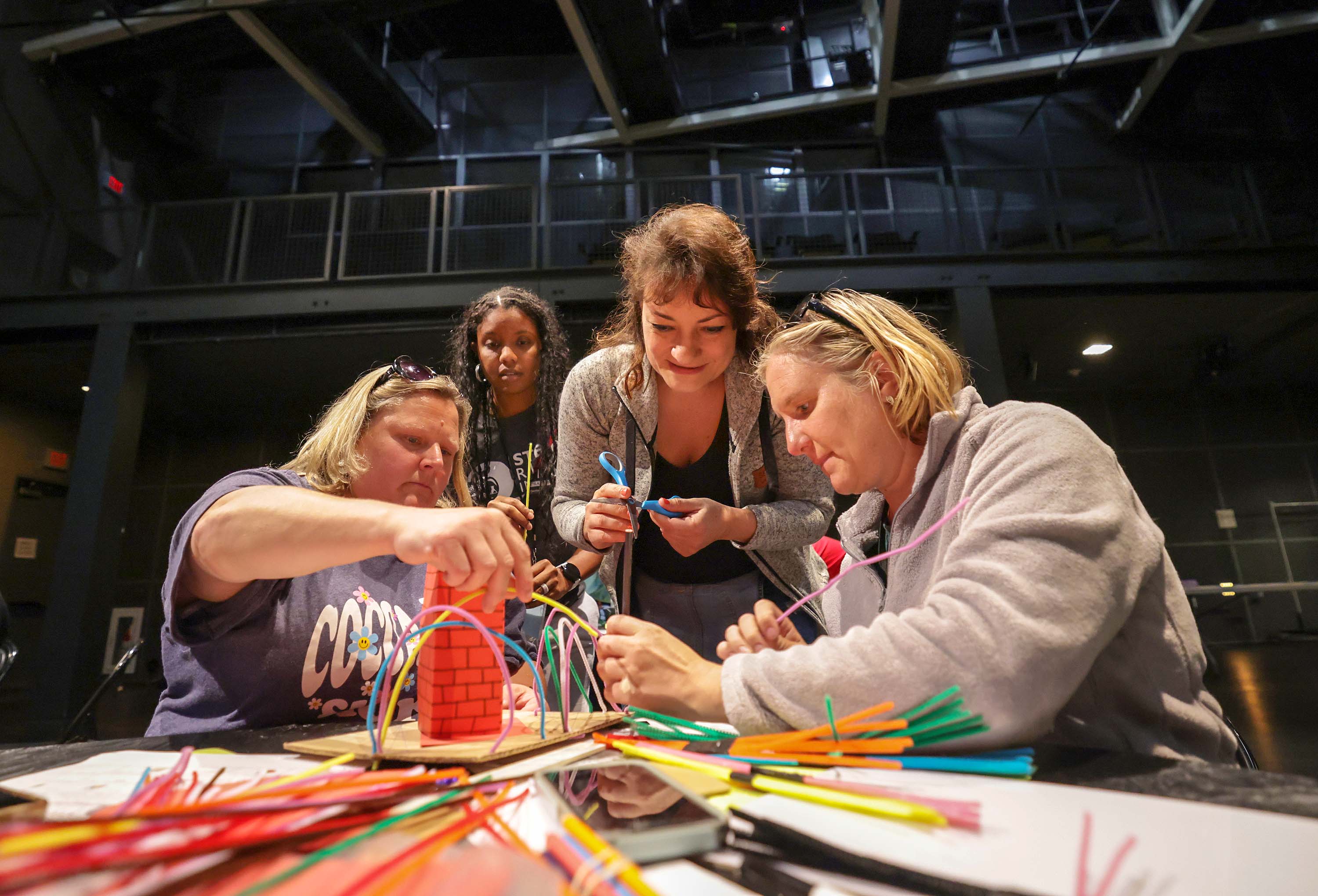 Four women huddle together to work on a paper sculpture.