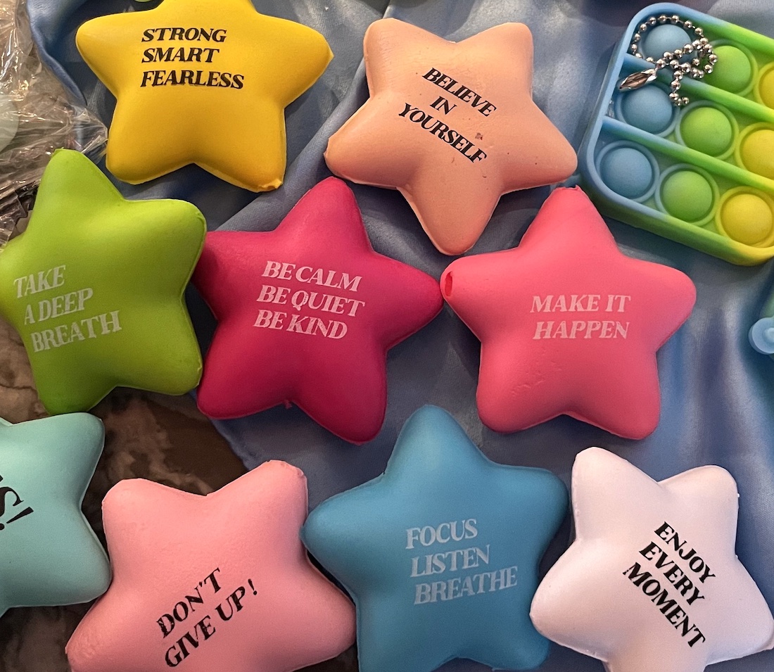 A collection of about 10 fidget toys. Most are colorful star-shaped stress balls with inspiring messages printed on them.