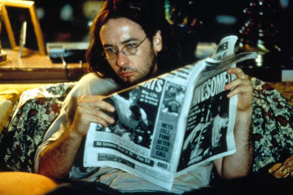 A man on a couch stares to his right as he holds a newspaper in his hands.