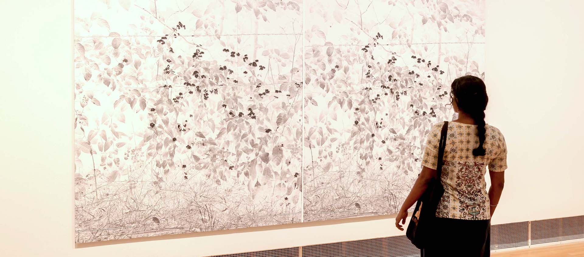 A woman looks at an artwork on a gallery wall.