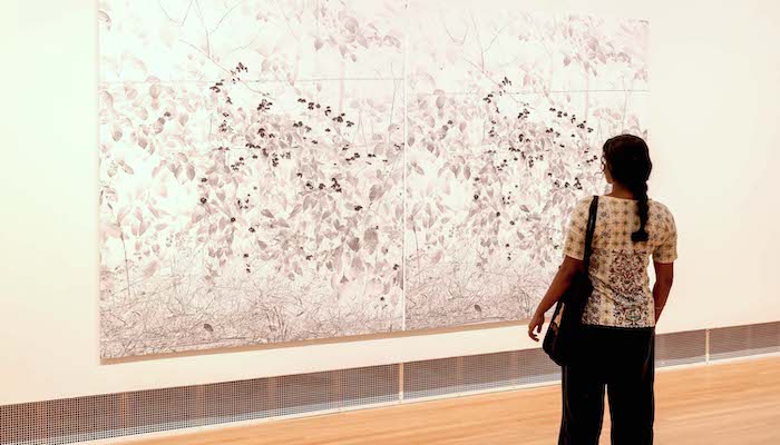A woman looks at an artwork on a gallery wall.