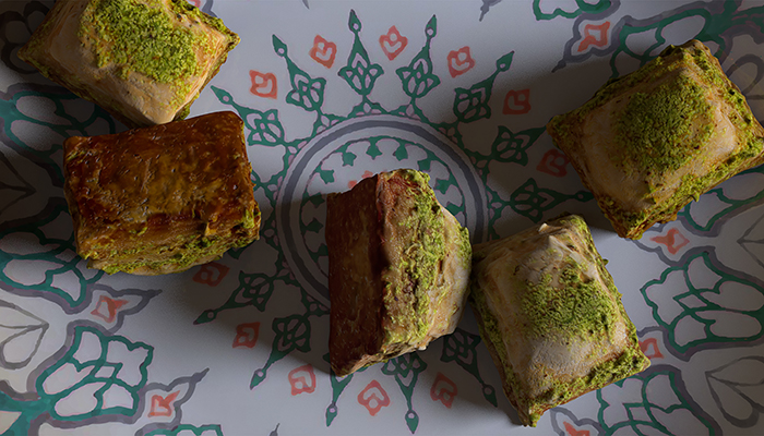 Close-up animated image of five pistachio baklava scattered across a white dish with painted decoration in green and orange.