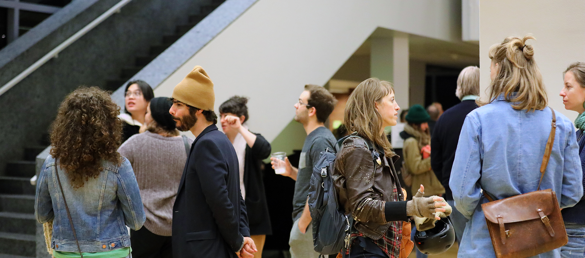 A group of people standing and mingling in the Wexner Center's lower lobby.
