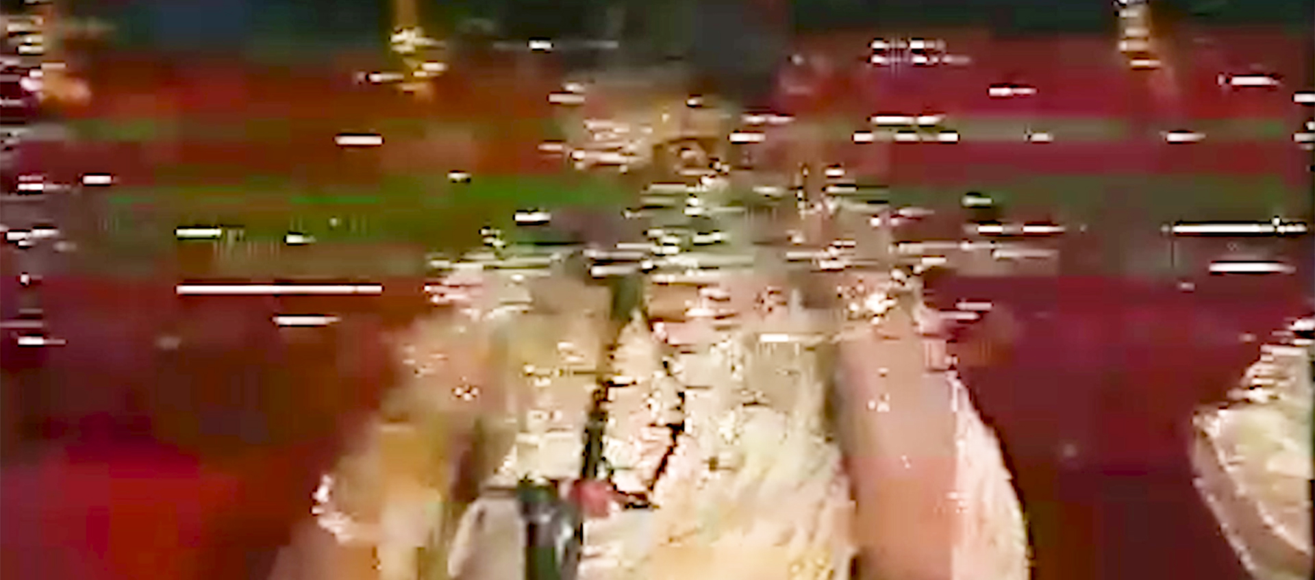 A distorted image from an old video tape shows a partially visible person in white clothing sitting on a red carpet.