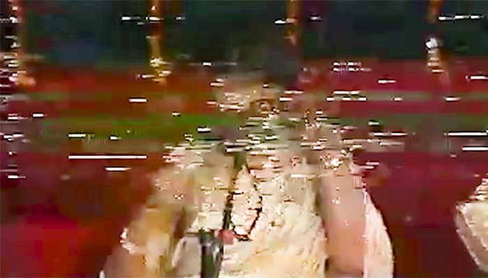 A distorted image from an old video tape shows a partially visible person in white clothing sitting on a red carpet