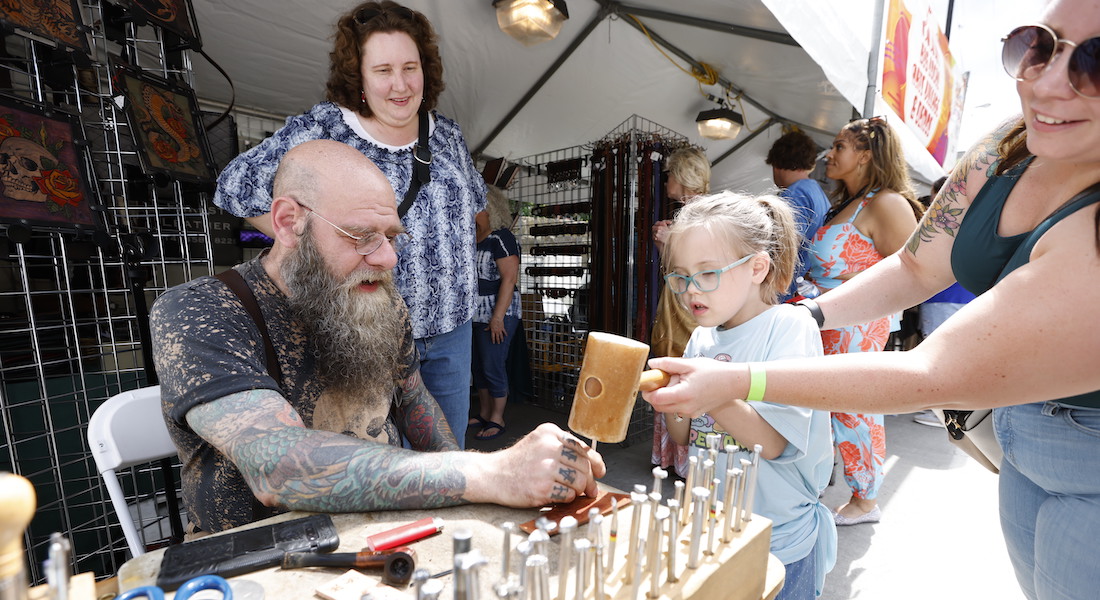 A man sits at the table and demonstrates how to work with leather stamping tools.