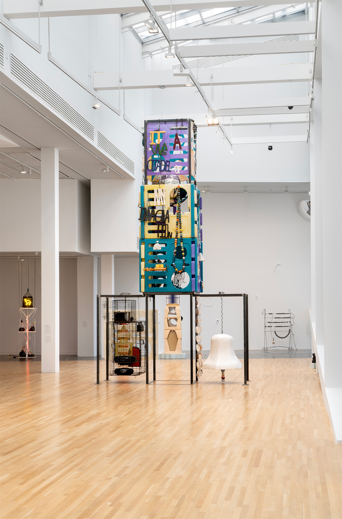 Upright, four-tier multicolored sculpture with ornaments, including text, beads, cages with radios, and ceramic bell, with ceramic pita curtain.
