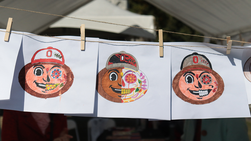 Three prints of Ohio State University’s mascot, Brutus, as a Day of the Dead figure are affixed to a clothesline.