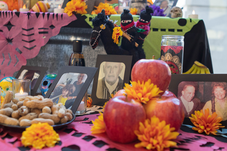 Apples, peanuts, orange flowers, candles, paper crafts, candy skulls, and framed photographs adorn a table.