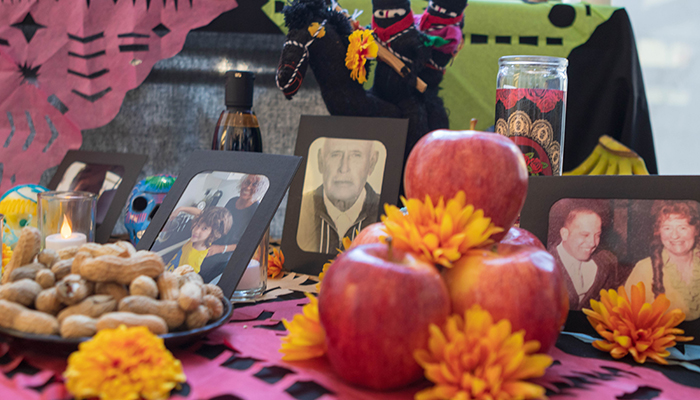 Apples, peanuts, orange flowers, candles, paper crafts, candy and decorative skulls, and framed photographs adorn a table.
