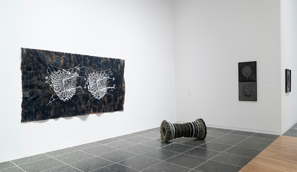 A polishing-wheel sculpture rests on the floor. On the two walls are a rectangular work with two spider webs and two stacked works. 