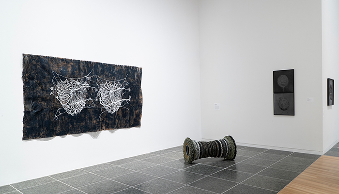 A polishing-wheel sculpture rests on the floor. On the two walls are a rectangular work with two spider webs and two stacked works. 