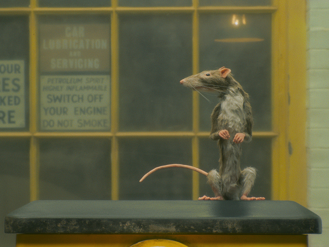 A lifelike rat puppet stands on its hind feet and looks to its right.