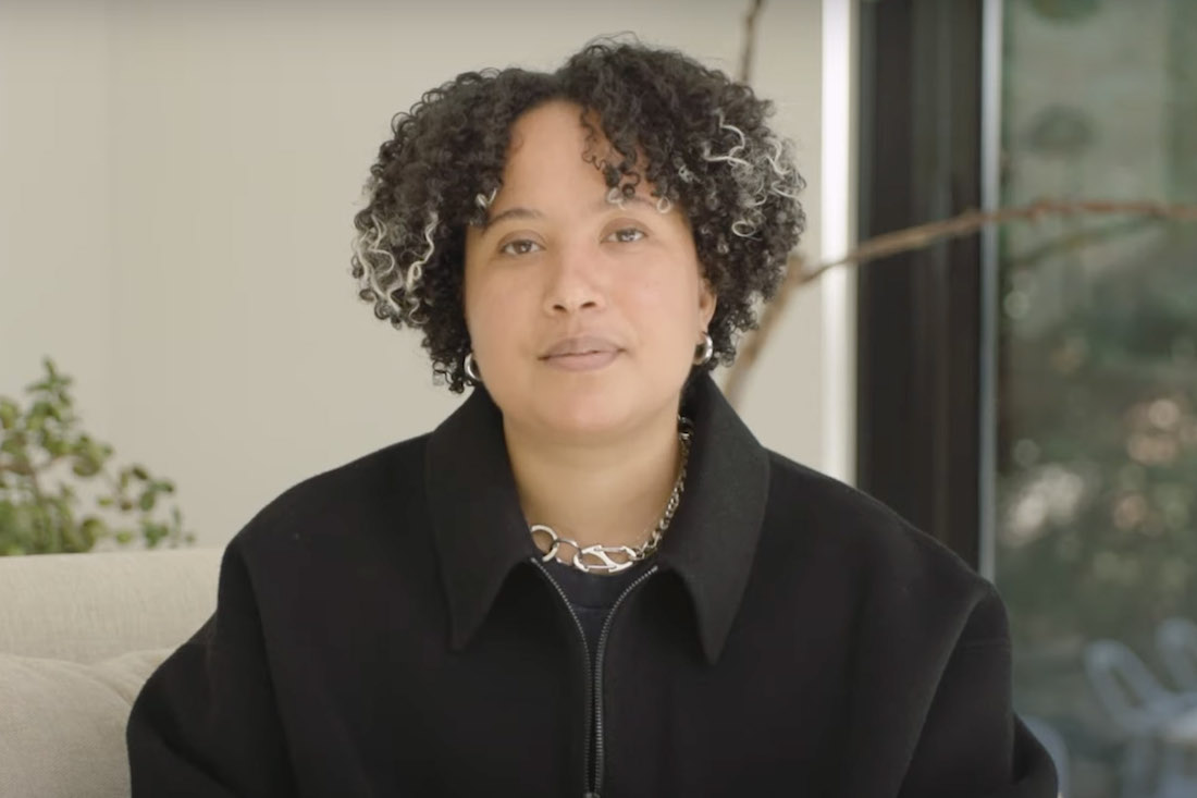 A woman with short curly hair sits and faces the camera