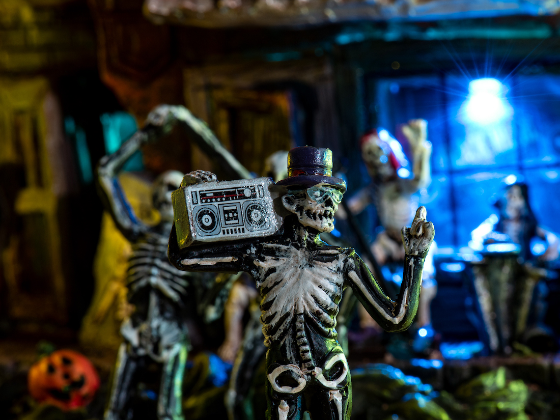 Close-up of a miniature skeleton holding a boom box in front of other skeletons in various poses.