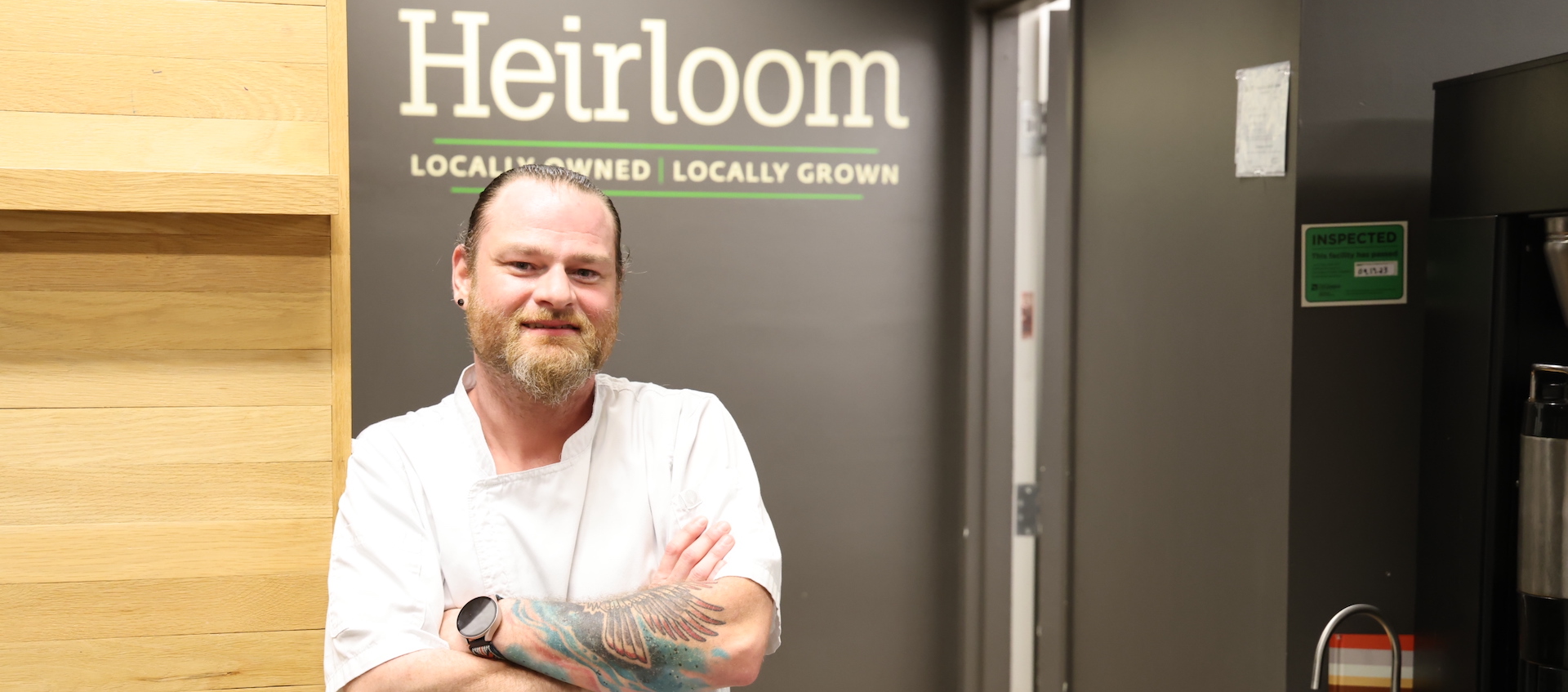 A man stands smiling in front of a wall sign for Heirloom Cafe.