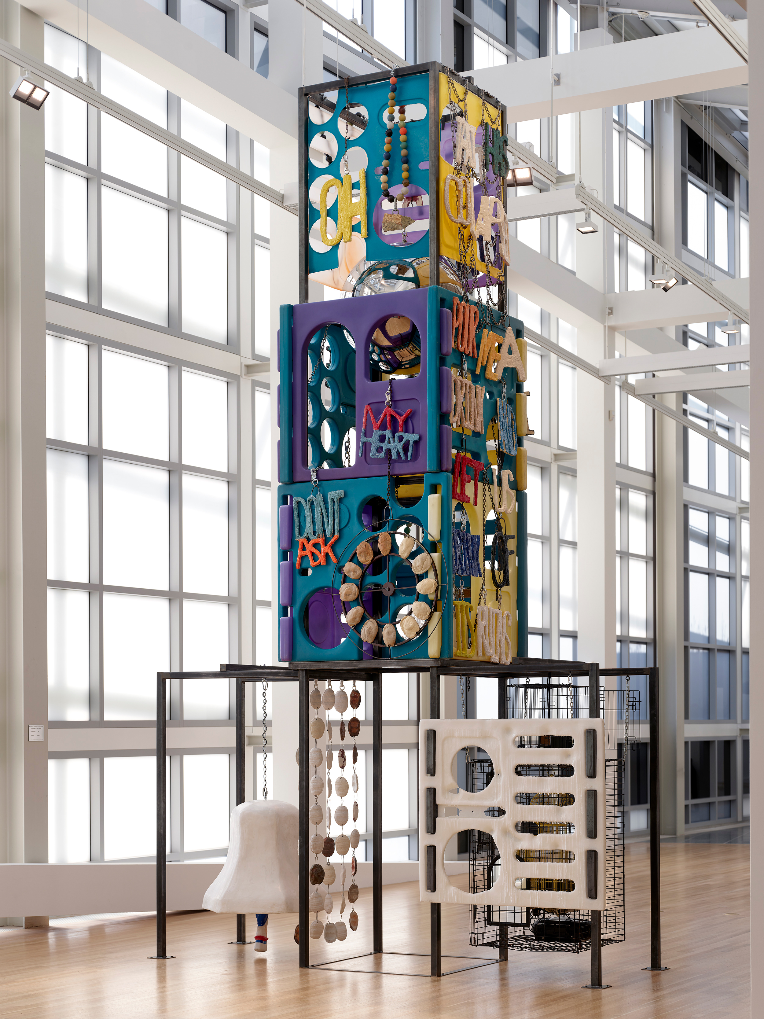 Upright, four-tier multicolored sculpture with ornaments, including text, beads, cages with radios, and ceramic bell with ceramic pita curtain.