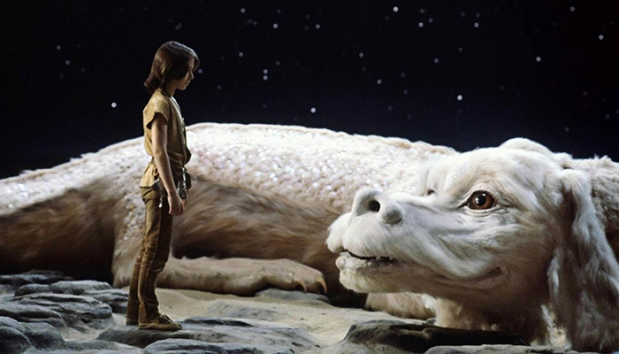 Under a starry sky, a young boy stands in front of a large, white mystical creature that resembles both a dragon and a shaggy dog. 