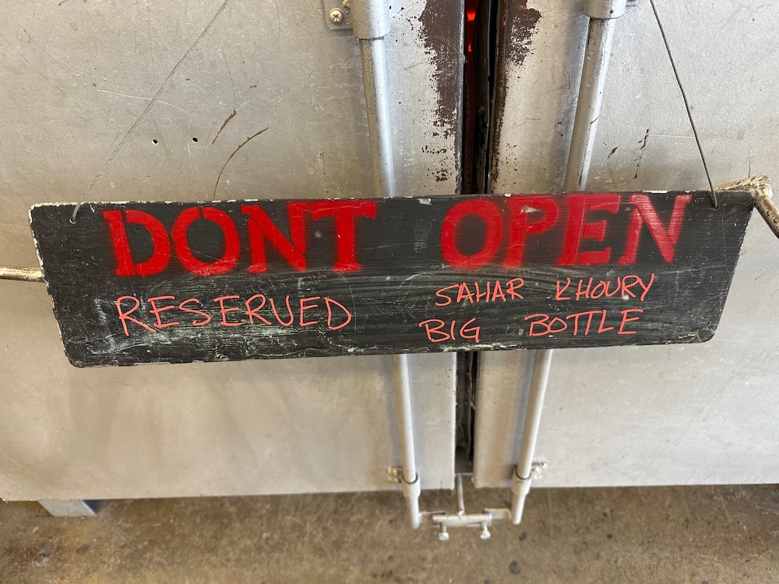 Working and storage space with a hand painted sign in front of the doors reading, “Don’t Open – Reserved. Sahar Khoury Big Bottle”
