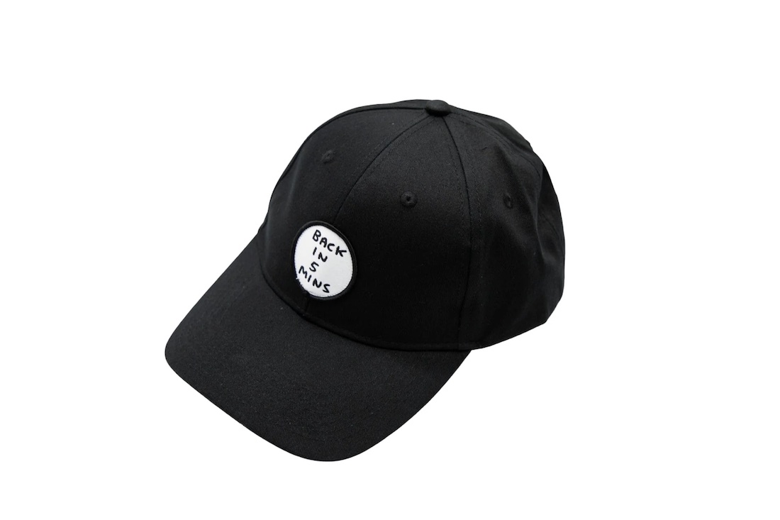 Black baseball cap with white patch on front that reads, "Back in 5 minutes"