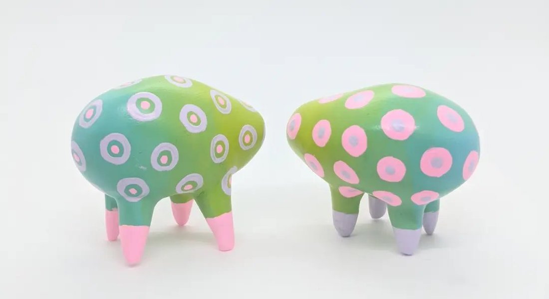 Two small cloud-shaped clay sculptures, each with four legs, are painted a pastel dot pattern.