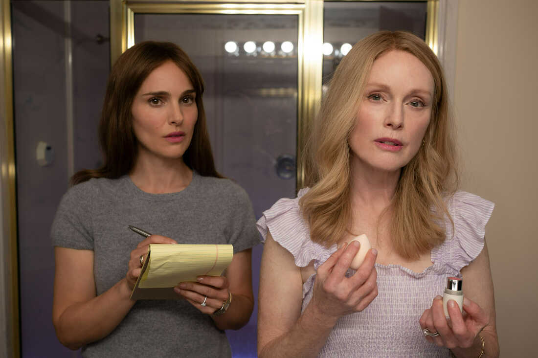 Two women stand together in a bathroom and look at the camera as if looking into a mirror.