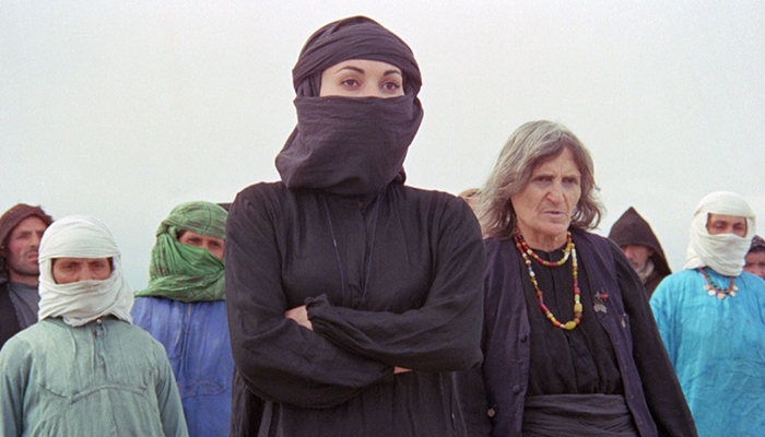 A group of people, some of whom are wearing head coverings. A woman in front is wearing all black with a head and face covering and her arms crossed.