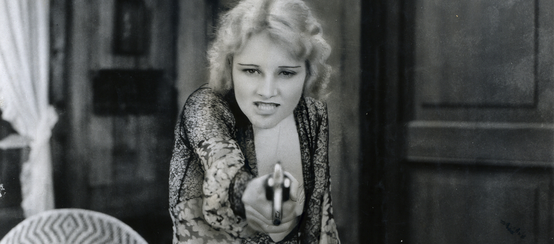 A black and white image of a woman wearing a flowered dress holding a gun.