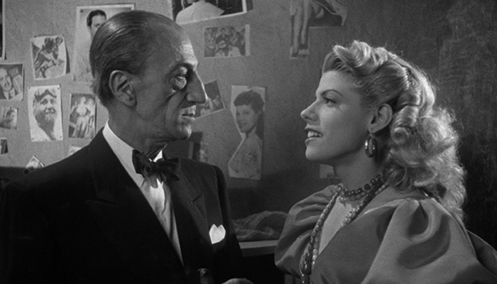 A black and white still from Victims of Sin showing a man and a woman facing each other in fancy dress.
