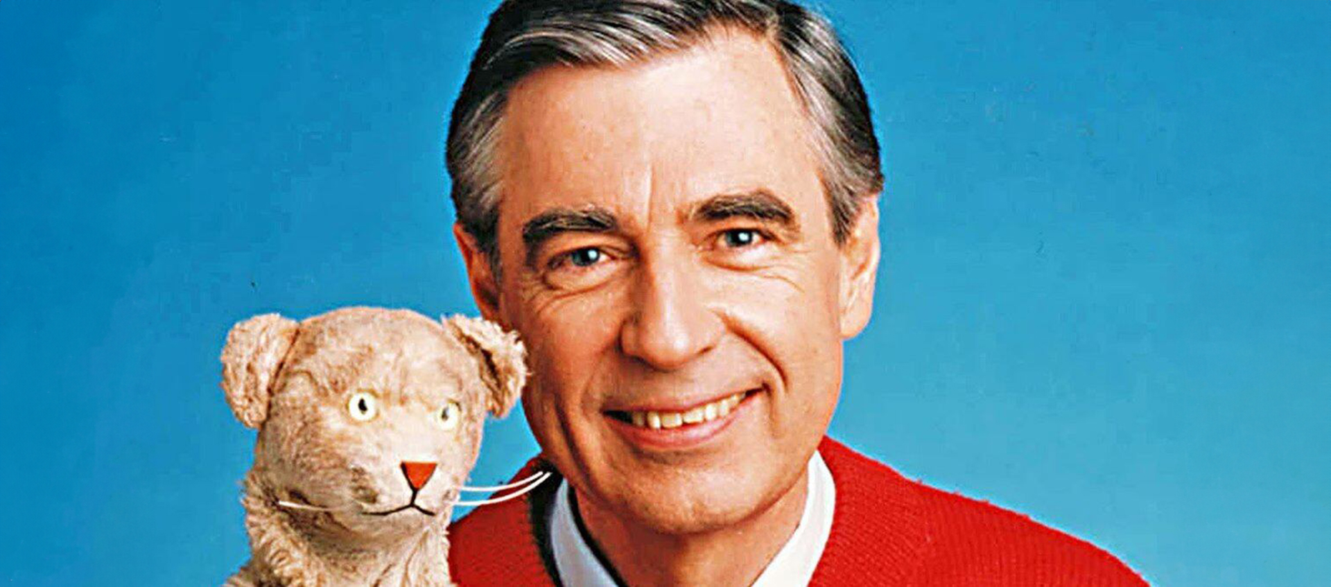 A headshot of Fred Rogers holding the puppet Daniel Tiger.