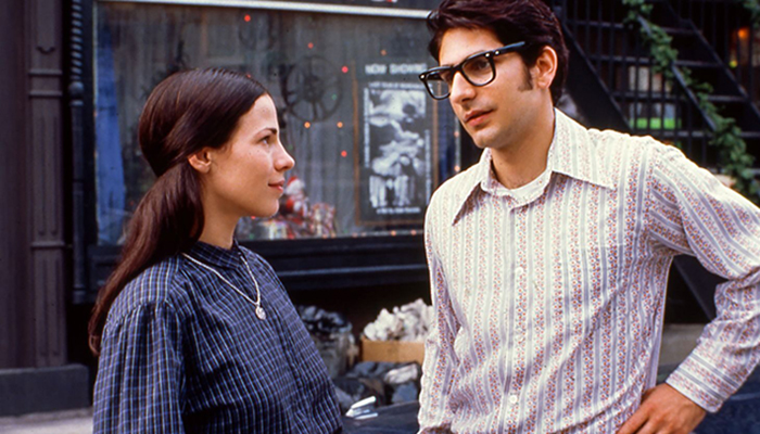 Still from the film Household Saints of a man and a woman standing on a city street looking at each other.