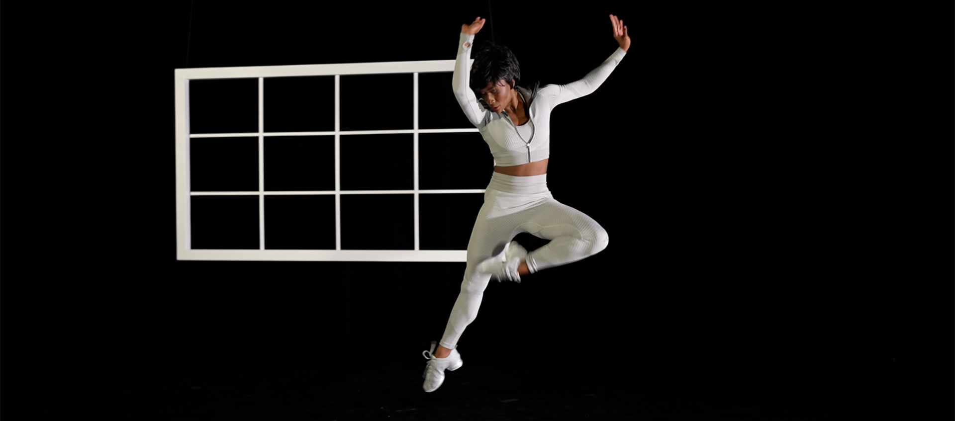 A woman jumping in the air on a black background with a white window behind her.