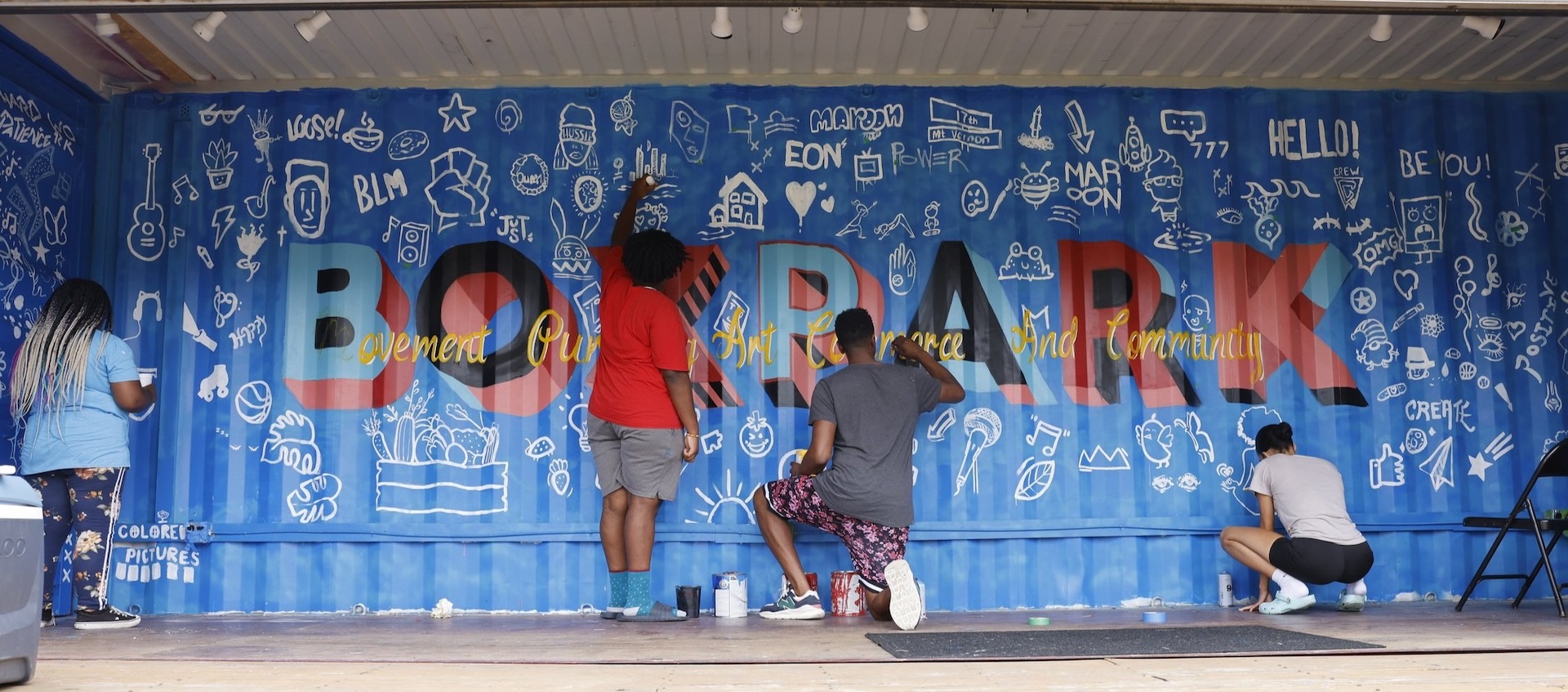 A few youths work on a mural on the inside wall of an outdoor shipping container