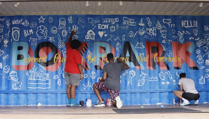 A few youths work on a mural on the inside wall of an outdoor shipping container