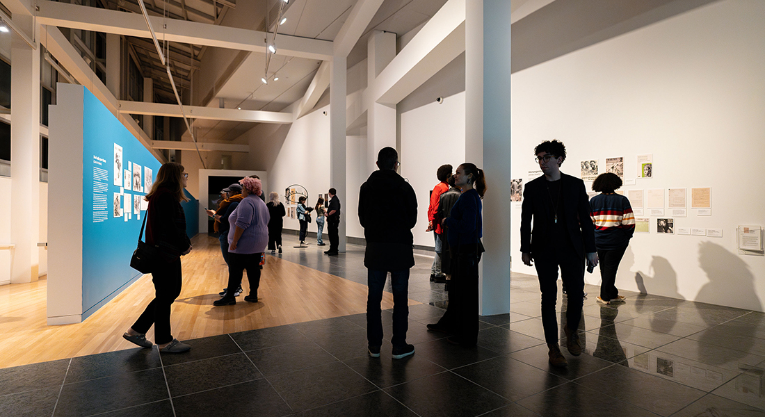 About 10 people walk around a contemporary gallery space, looking at an exhibition.