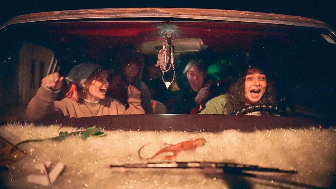 Four young people sit together in a car, smiling and cheering.