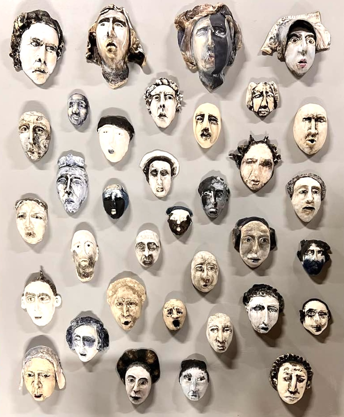 A neutral color wall is filled with about three dozen small ceramic sculptures of different heads.