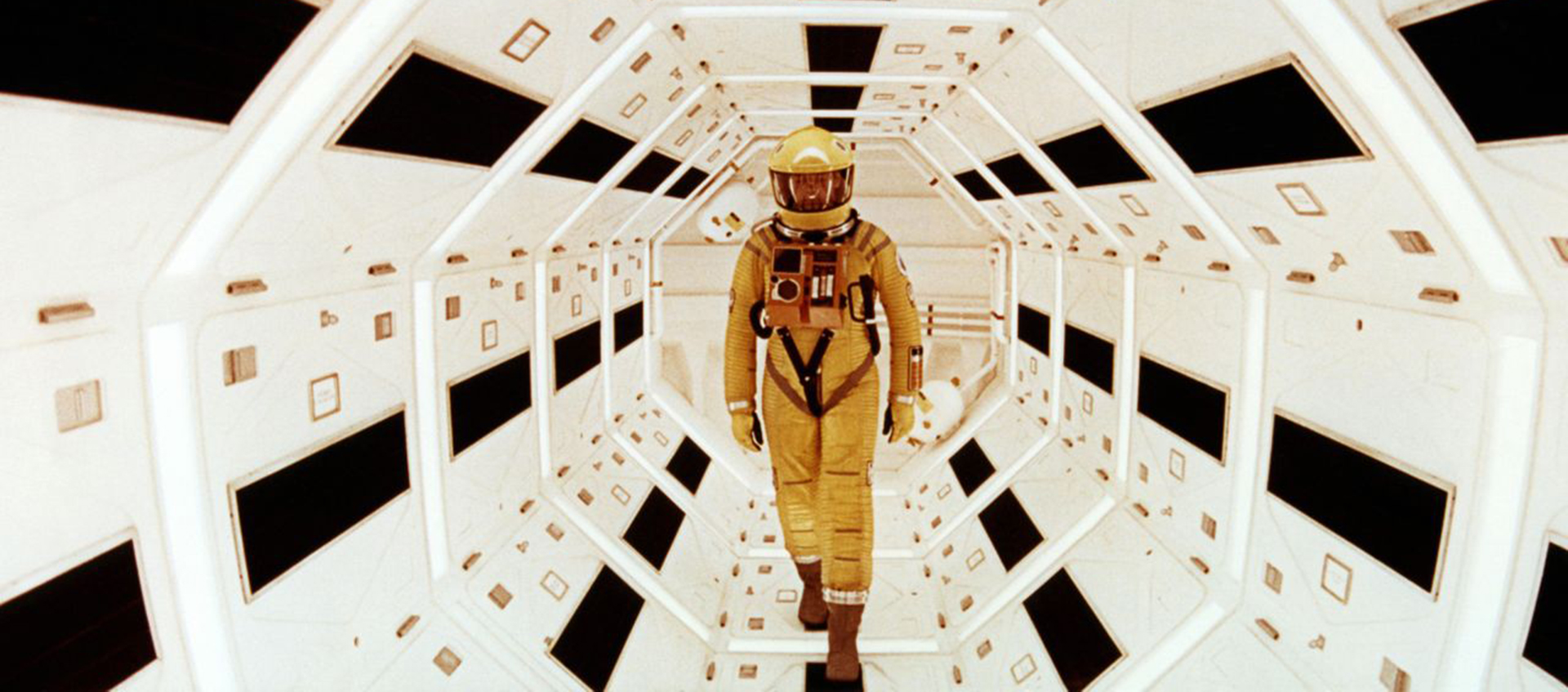 A figure in a yellow space suit stands in a tunnel with white panels.