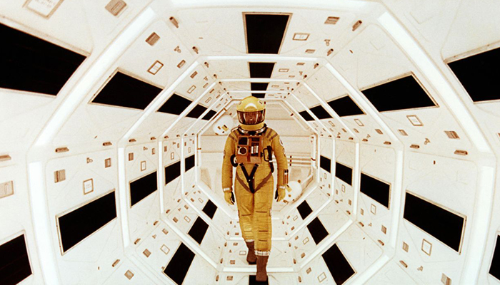 A figure in a yellow space suit stands in a tunnel with white panels.